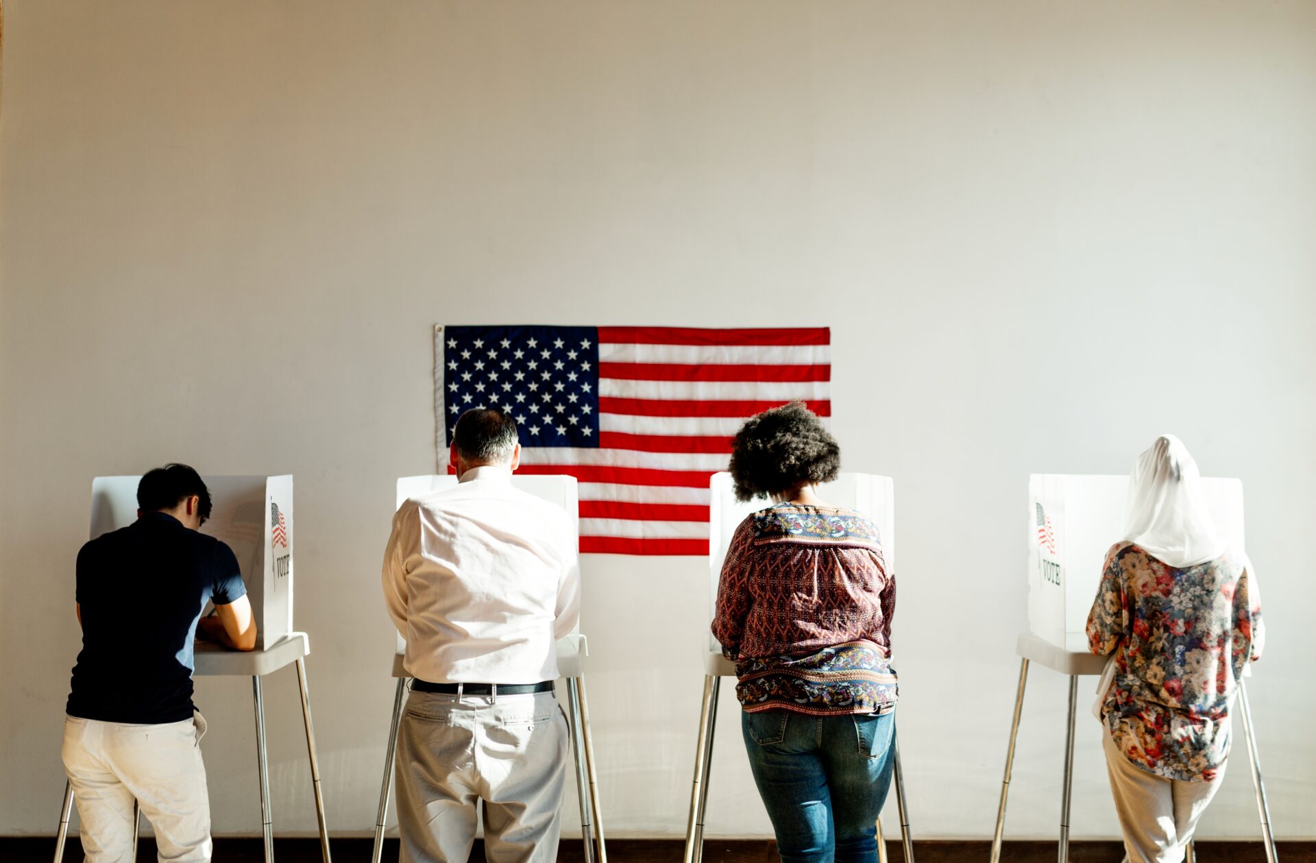 Diverse,American,Citizens,Voting,In,Booths,With,An,American,Flag