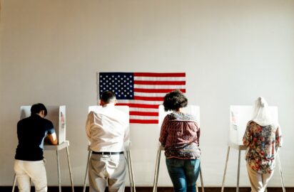 Diverse,American,Citizens,Voting,In,Booths,With,An,American,Flag