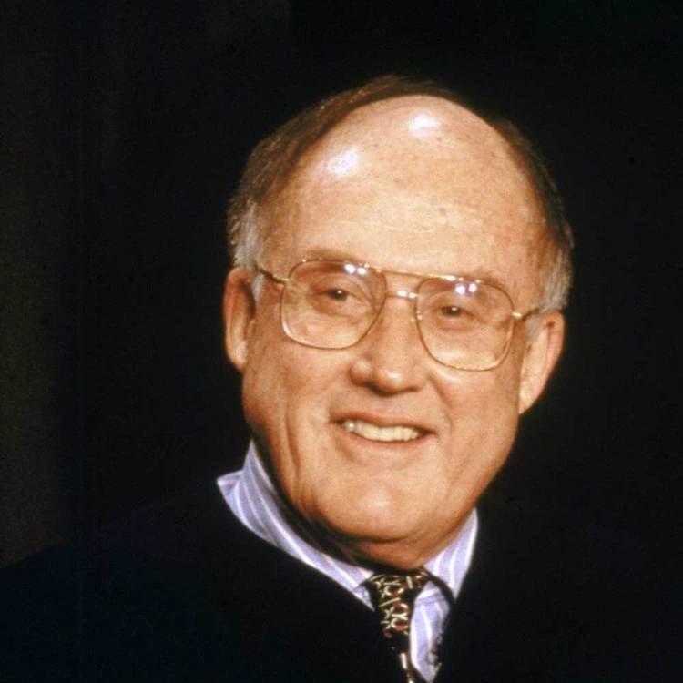 Portrait of a senior man with glasses, smiling, in professional attire.