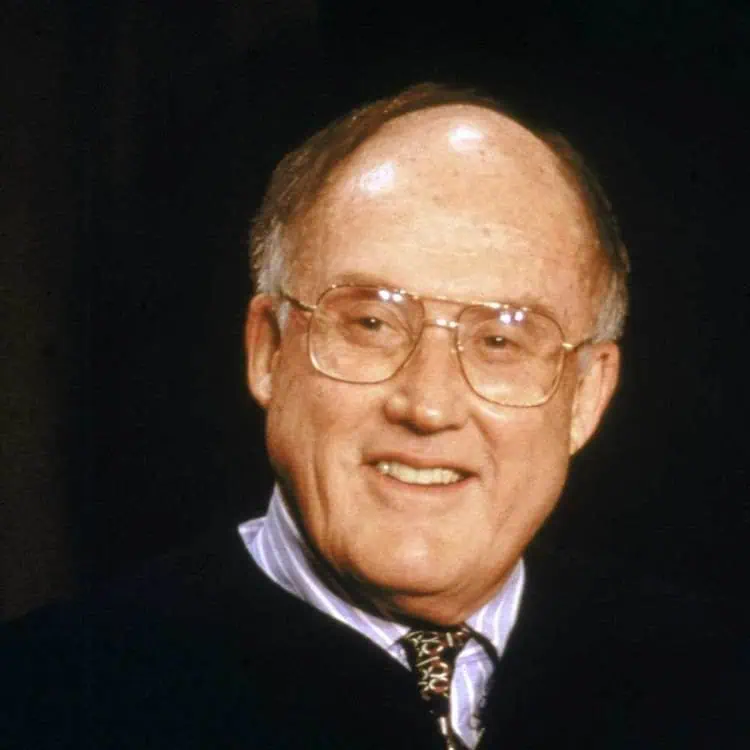 Portrait of a senior man with glasses, smiling, in professional attire.