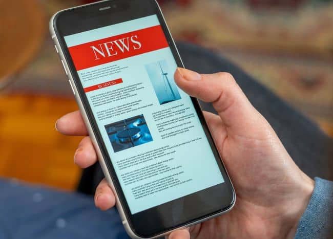 Person holding smartphone displaying news article on screen.